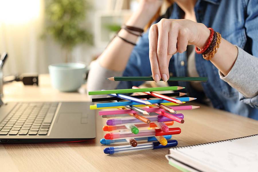 A woman sitting at her desk builds a tower of pens next to her computer.