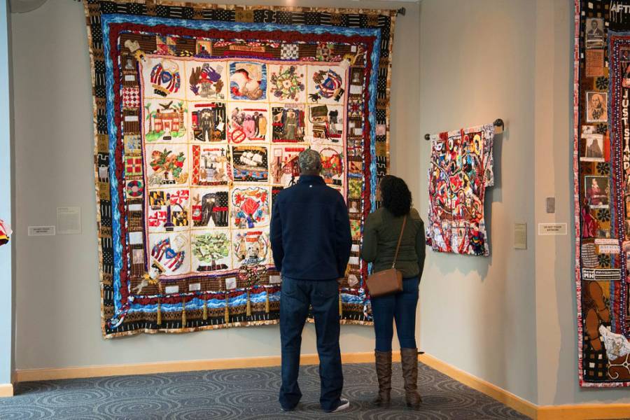 Two people stand in front of a quilt