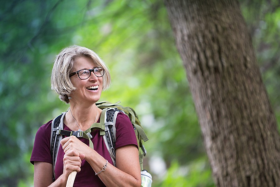 A happy middle-aged woman in hiking gear is enjoying the woods