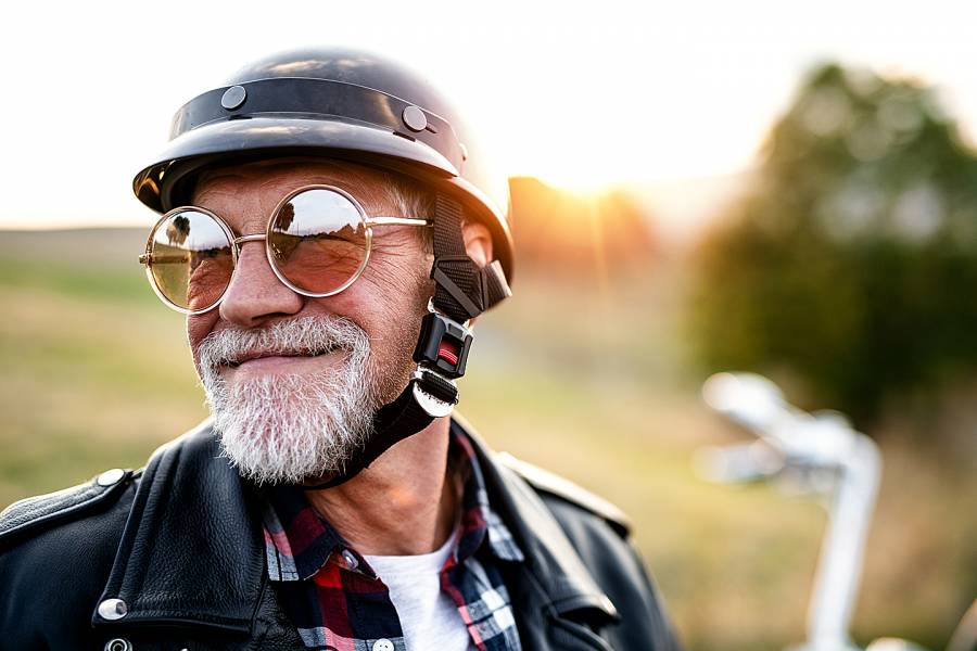 Senior man with beard, sunglasses, and helmet on a motorcycle