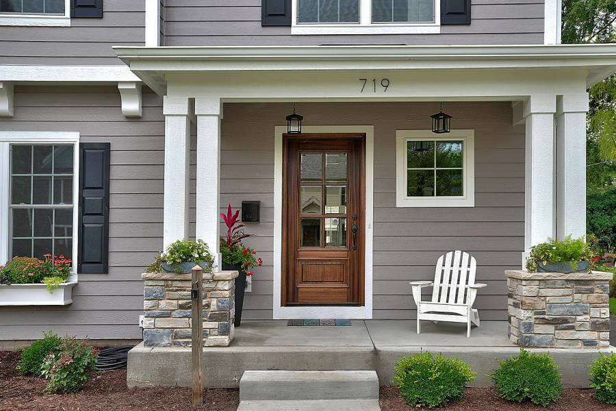 Welcoming front entrance to house has a chair and plants on porch