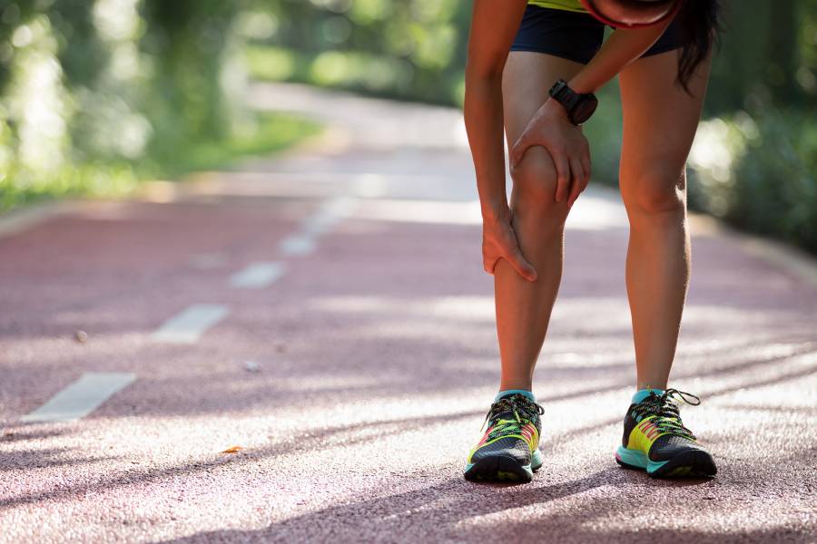 A runner pauses and holds her leg in pain