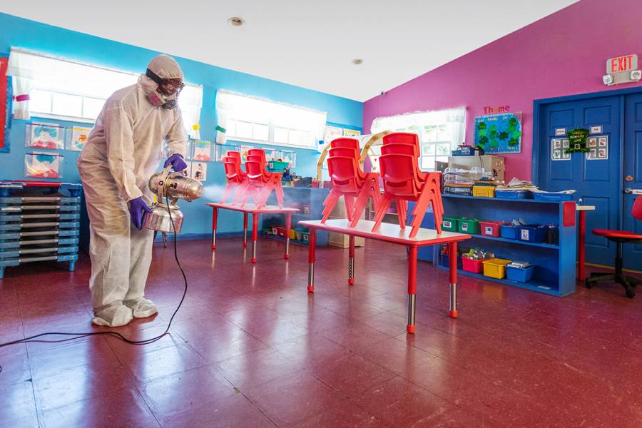 A masked custodian cleans a classroom