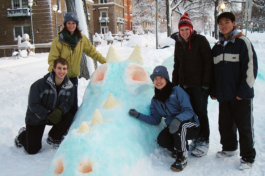 A group of students pose beside a snow dragon dyed blue with orange eyes