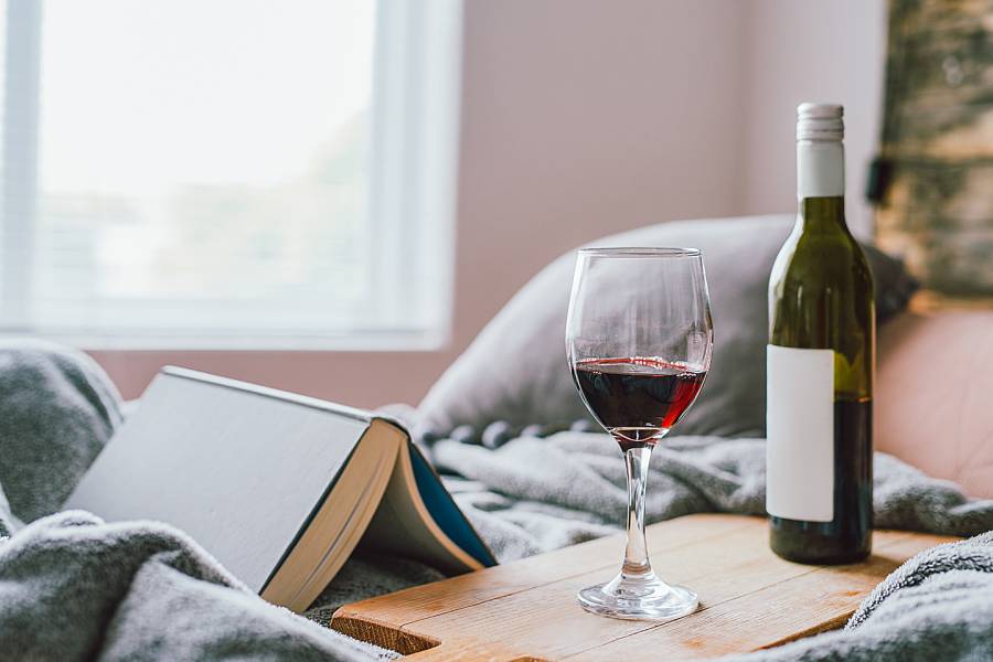 Bottle of wine and a glass near an open book on a bed