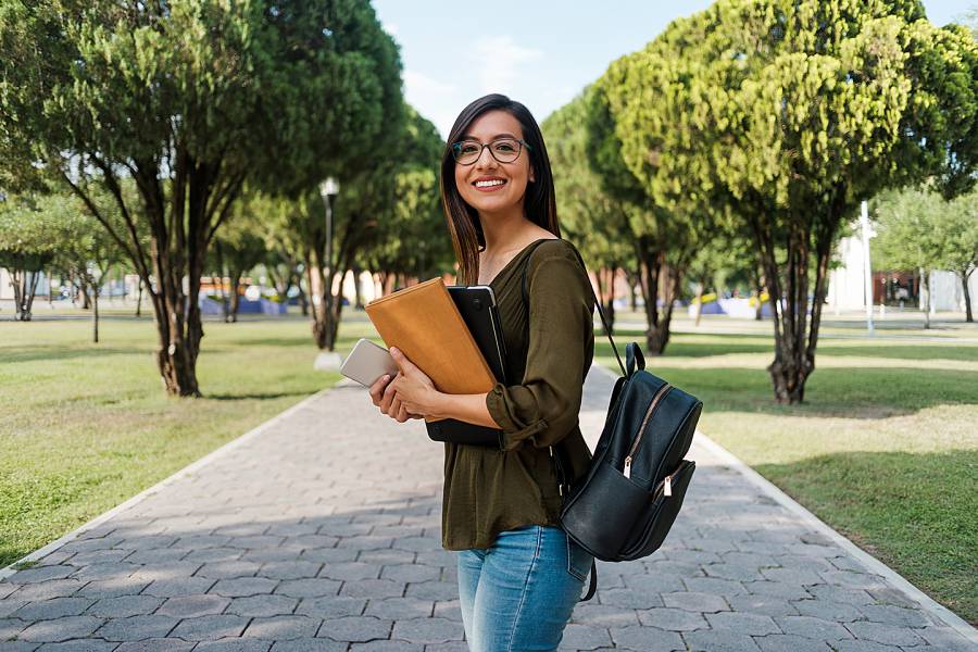 Smiling young woman holding books on a college campus