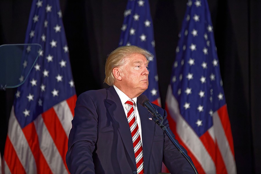 Donald Trump in front of three American flags