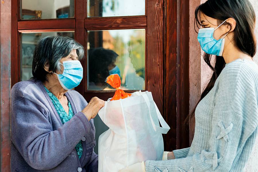 Young woman delivering groceries to an elderly woman, both of them wearing facial masks