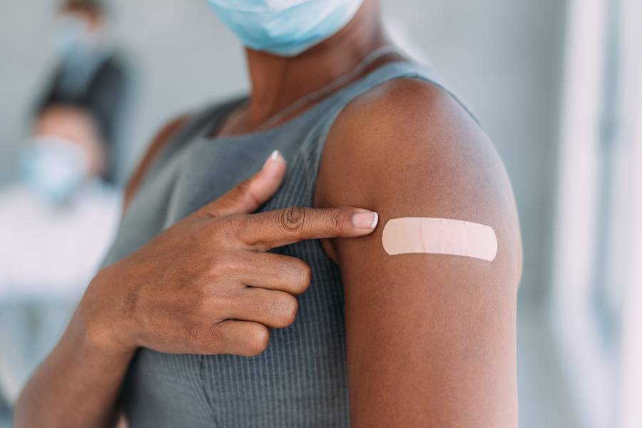 A woman points to a bandage covering her COVID-19 vaccine