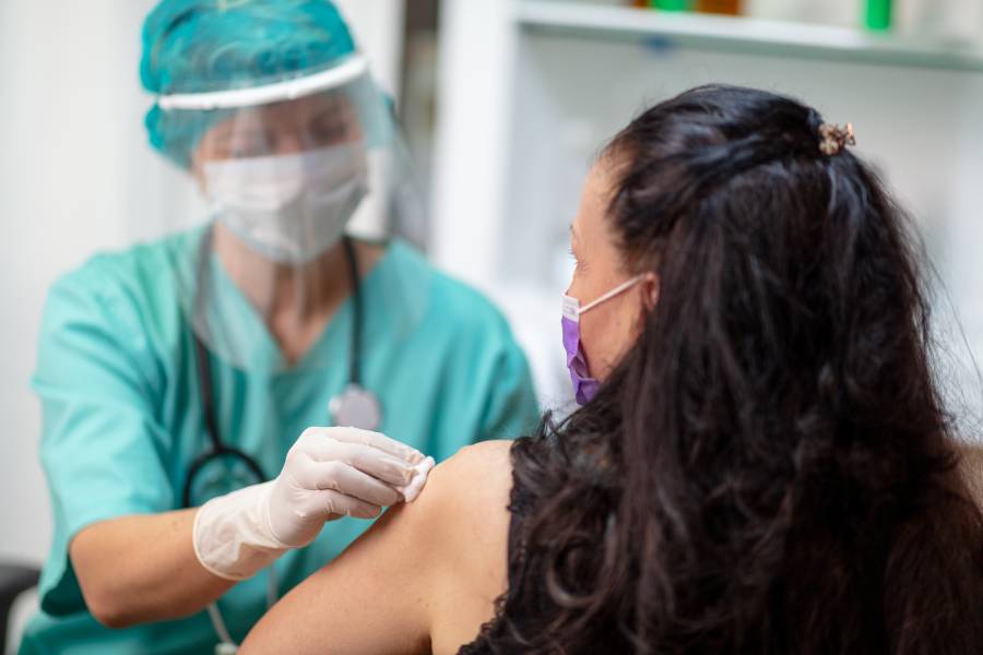 A nurse administers a shot to a masked woman