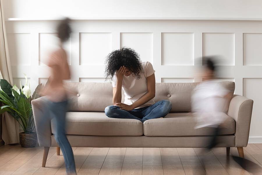 Stressed-looking woman on couch with children playing nearby