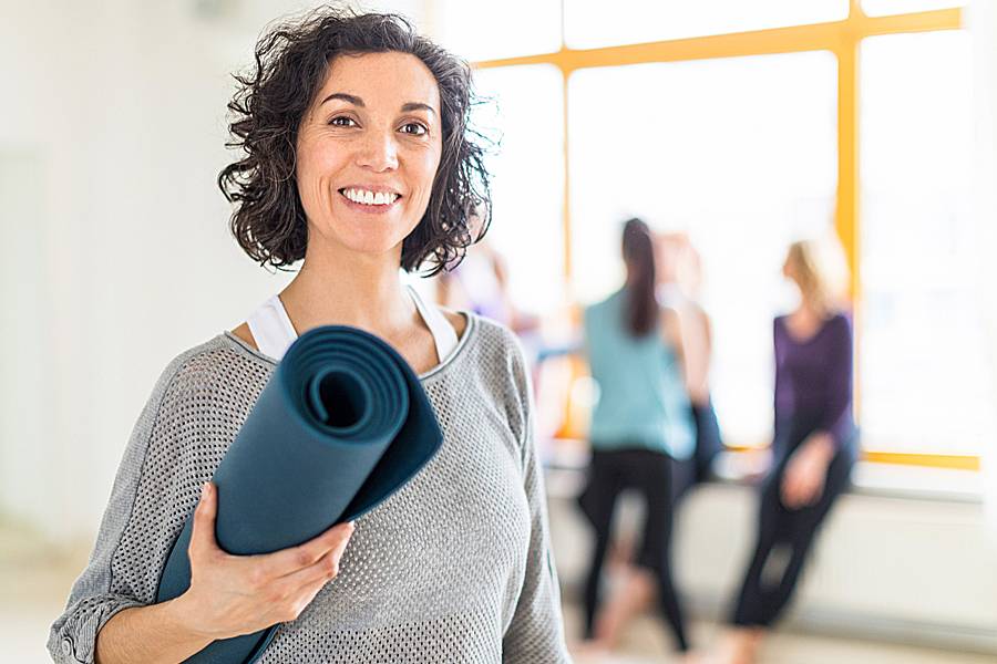 Smiling woman carrying a yoga mat in an exercise room