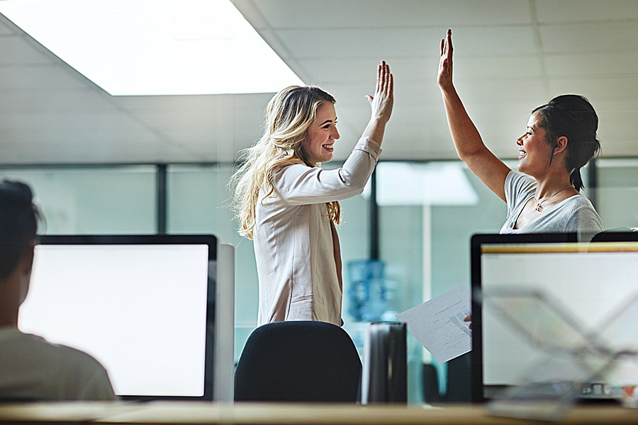 Two businesswomen high five in the office.