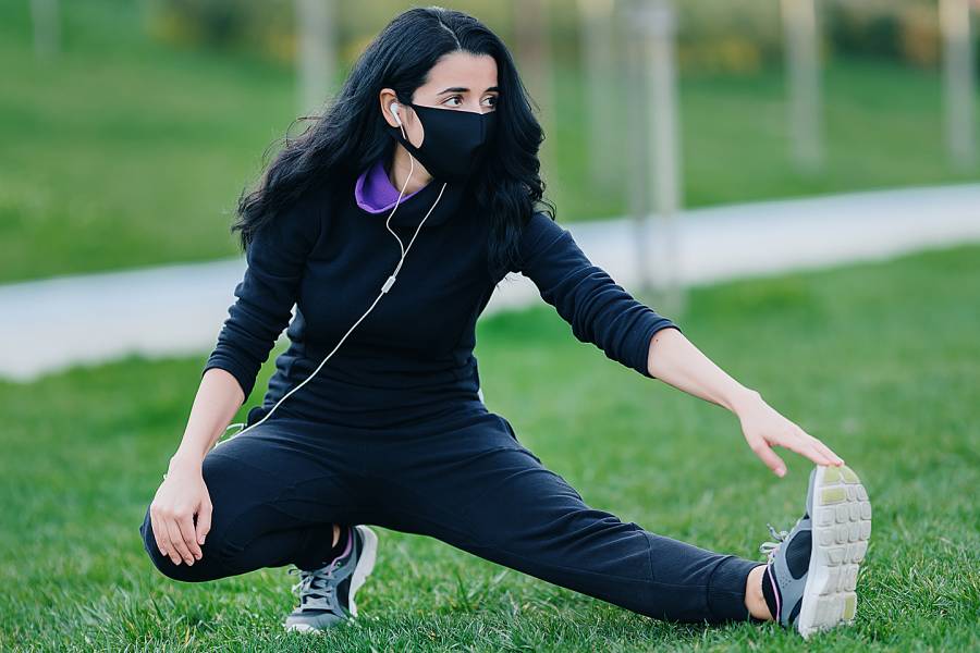 Young woman wearing mask and stretching on grass