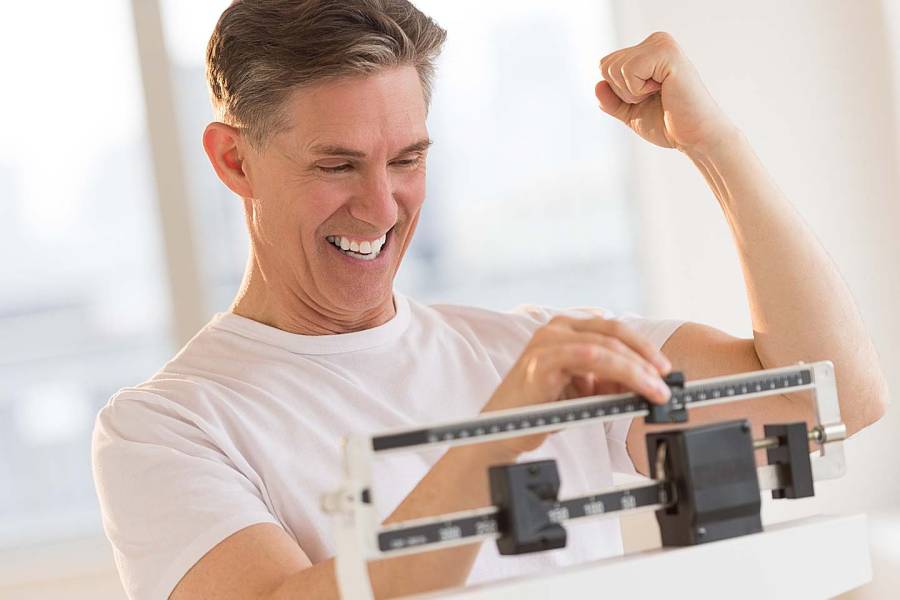 Mature man clenching fist excitedly while using balance weight scale at gym