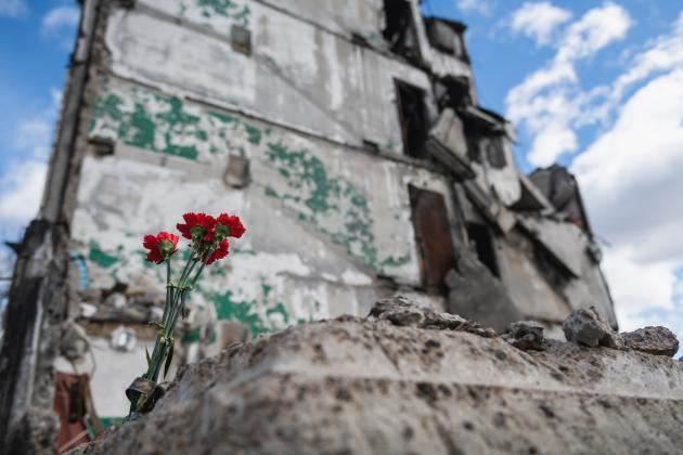 Four red flowers are seen in front of the cement remains of a multistory building in Ukraine