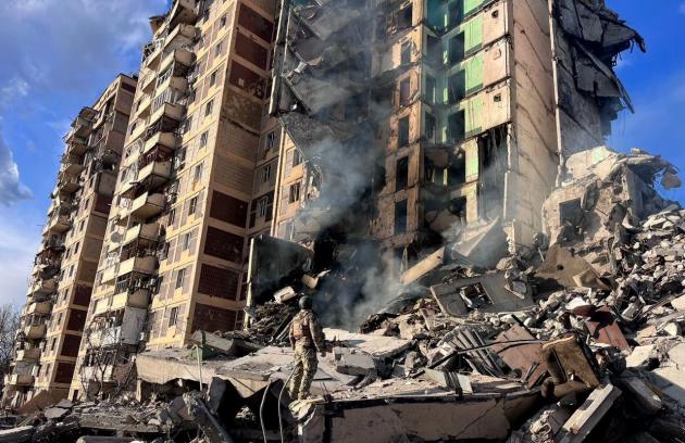 A soldier stands in front of a bombed apartment building.