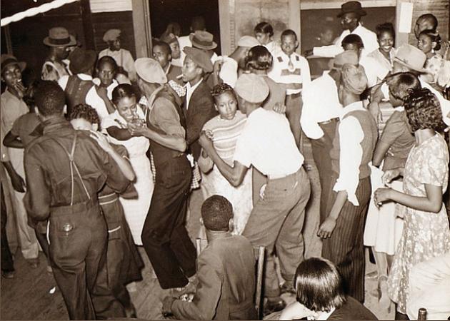 A black-and-white photo of African Americans dancing at a party in the early 1900s.