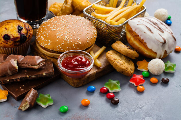 an assortment of unhealthy foods on a table, including a hamburger, fries, candy, chocolate, soda, and a donut