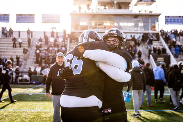 Two football players in black jerseys hug