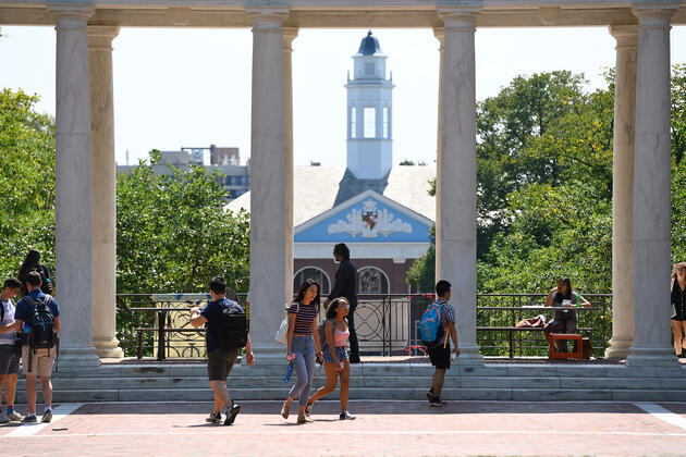 Students walk past columns on a sun-drenched campus quad