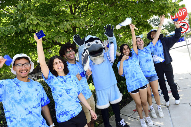 A group of student volunteers in blue tie-dye shirts pose with Jay, the mascot