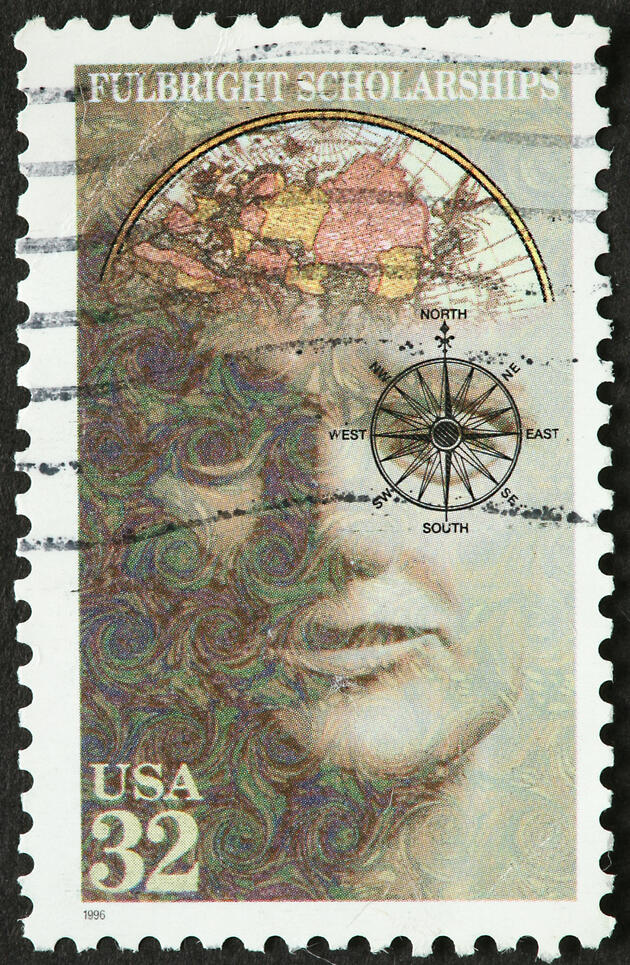 A used stamp that reads "Fulbright Scholarships, USA 32." On it is an abstract depiction of a man with a map in his brain and a compass over his eye.