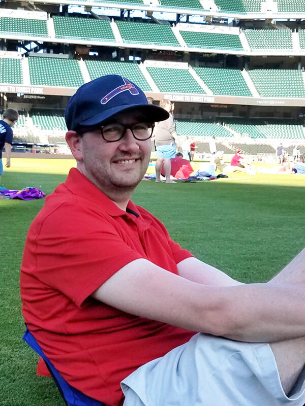 A man in a red shirt and Atlanta Braves hat sits on the baseball field at Atlanta's Truist Park