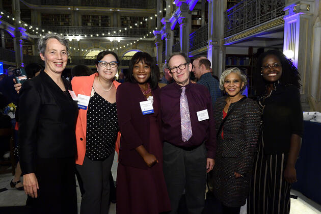 Six people smile for a photo during a party at the Peabody Library.