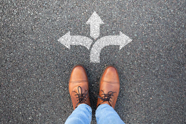 Man's feet standing on pavement in front or arrows pointing in three directions