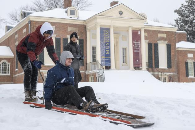 A group of college students get ready to send one of their own down a snowy hill on a sled.