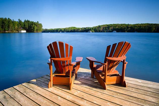 Two lounge chairs on a dock facing toward a beautiful lake