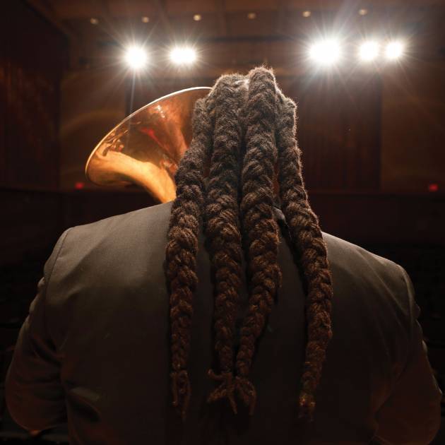 a photograph of tubist Richard White on stage, holding a tuba, shot from behind