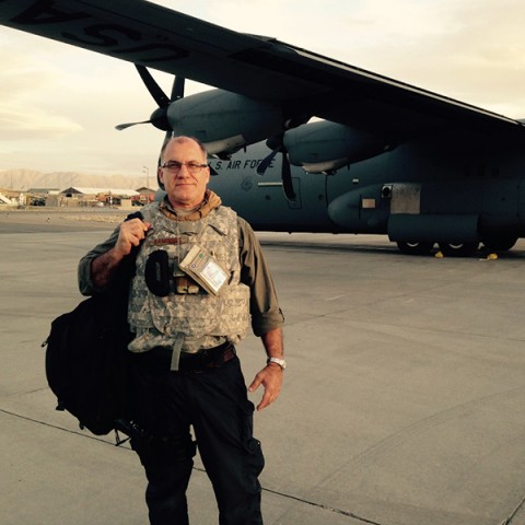 A man in a military flak vest holds bags in front of a Air Force plane